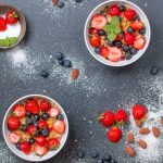 Top view of fresh berry and almond bowls with sugar on dark slate.