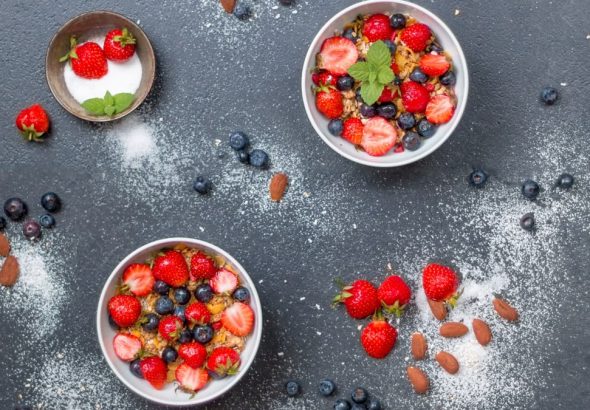 Top view of fresh berry and almond bowls with sugar on dark slate.