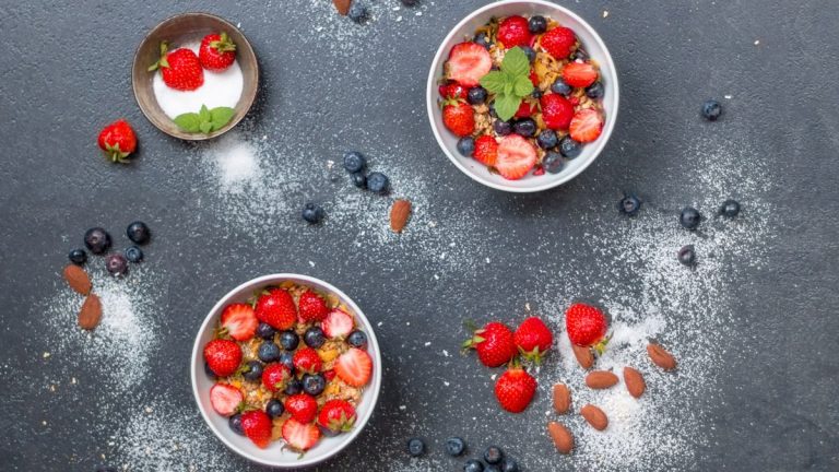 Top view of fresh berry and almond bowls with sugar on dark slate.